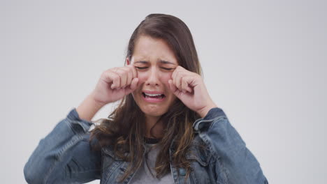 an attractive young woman crying against a grey