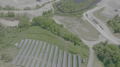 Drone-high-angle-solar-panels-in-foreground,-high-angle-truck-pulling-into-sandpit