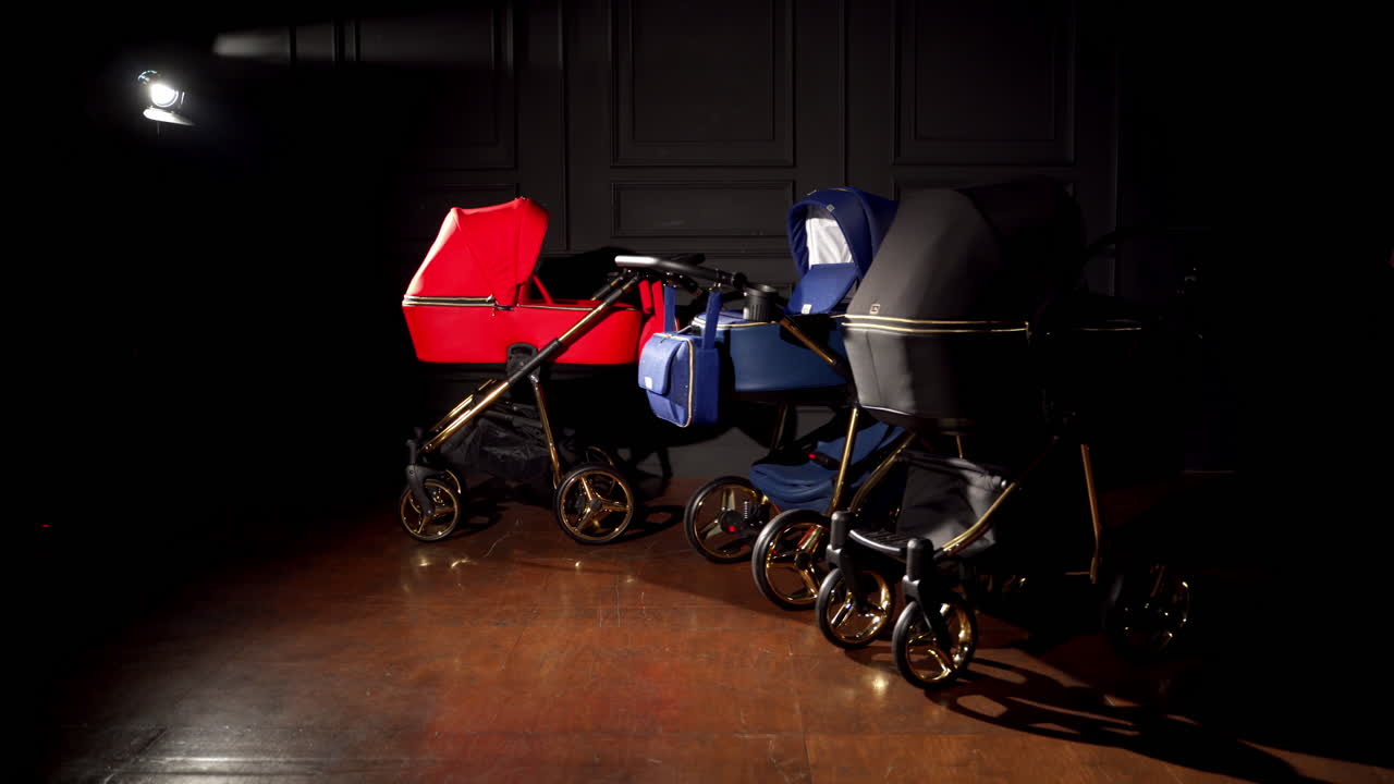 New red, blue and black baby prams in a dark room. Modern strollers presentation in one lamp light.