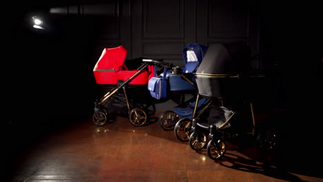 new red, blue and black baby prams in a dark room. modern strollers presentation in one lamp light.
