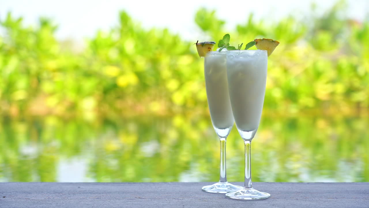 Two white Cocktail Drinks with Pineapple By A Swimming Pool day time