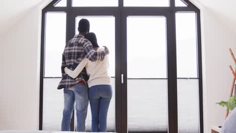 Rear-view-of-happy-african-american-couple-embracing-in-front-of-window-at-home,-in-slow-motion