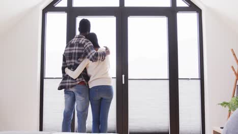 rear view of happy african american couple embracing in front of window at home, in slow motion