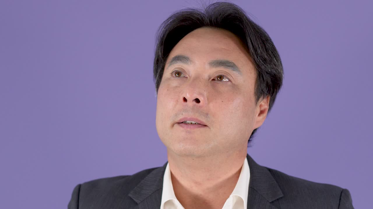 スーツを着た中年ビジネスマンが物思いにふけりながら思案している様子、わずかな頭の動き、スタジオ照明、固定カメラ。
