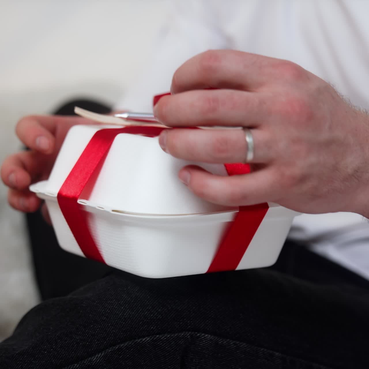 Food box with red ribbon and fork. Male hand take the box and pulls the ribbon to untie it. Close up