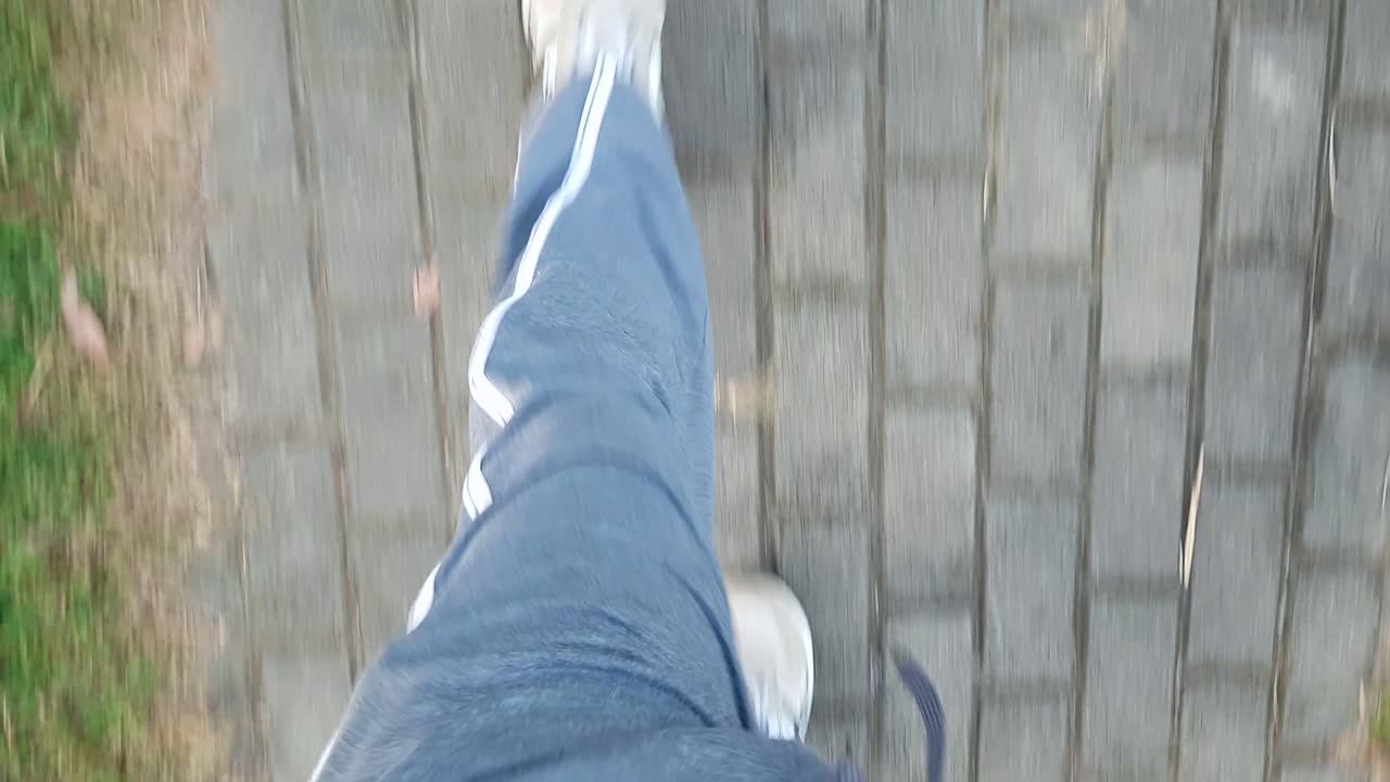 hand held shot of man in white shoes gray sportswear pants walking in a pavement sidewalk view from above waist level