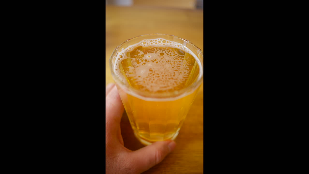 Vista dall'alto di un bicchiere di birra lager chiara appena versato, con bolle di schiuma, su un tavolo di legno. Verticale.