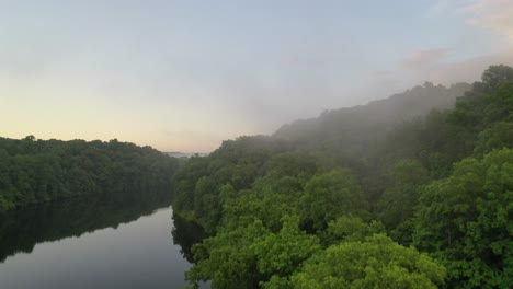 Flying-directly-though-rising-mist-from-river-surrounded-by-dense-forest