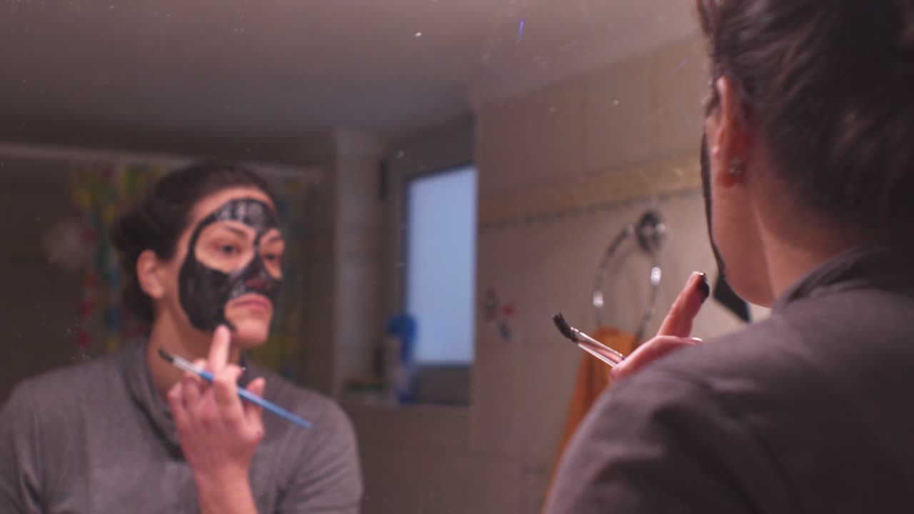 joven mujer caucásica aplicando mascarilla de belleza negra en su cara en casa