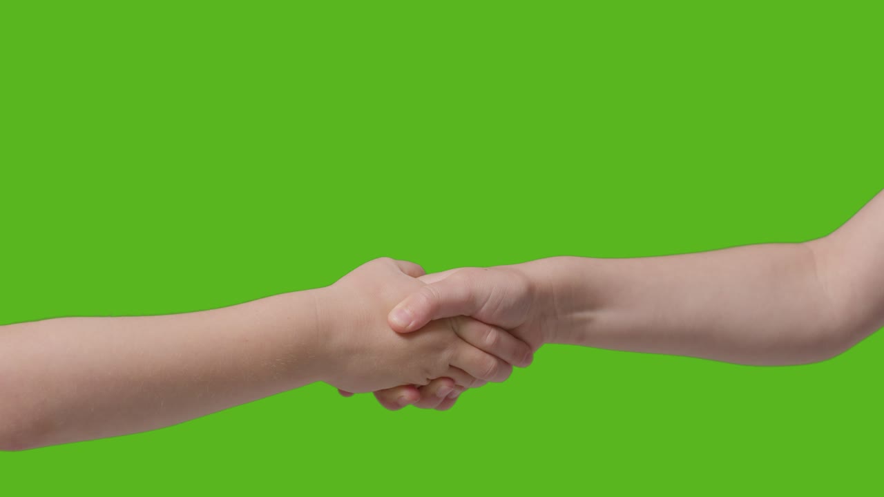 Close Up Of Two Young Children Shaking Hands Against Green Screen