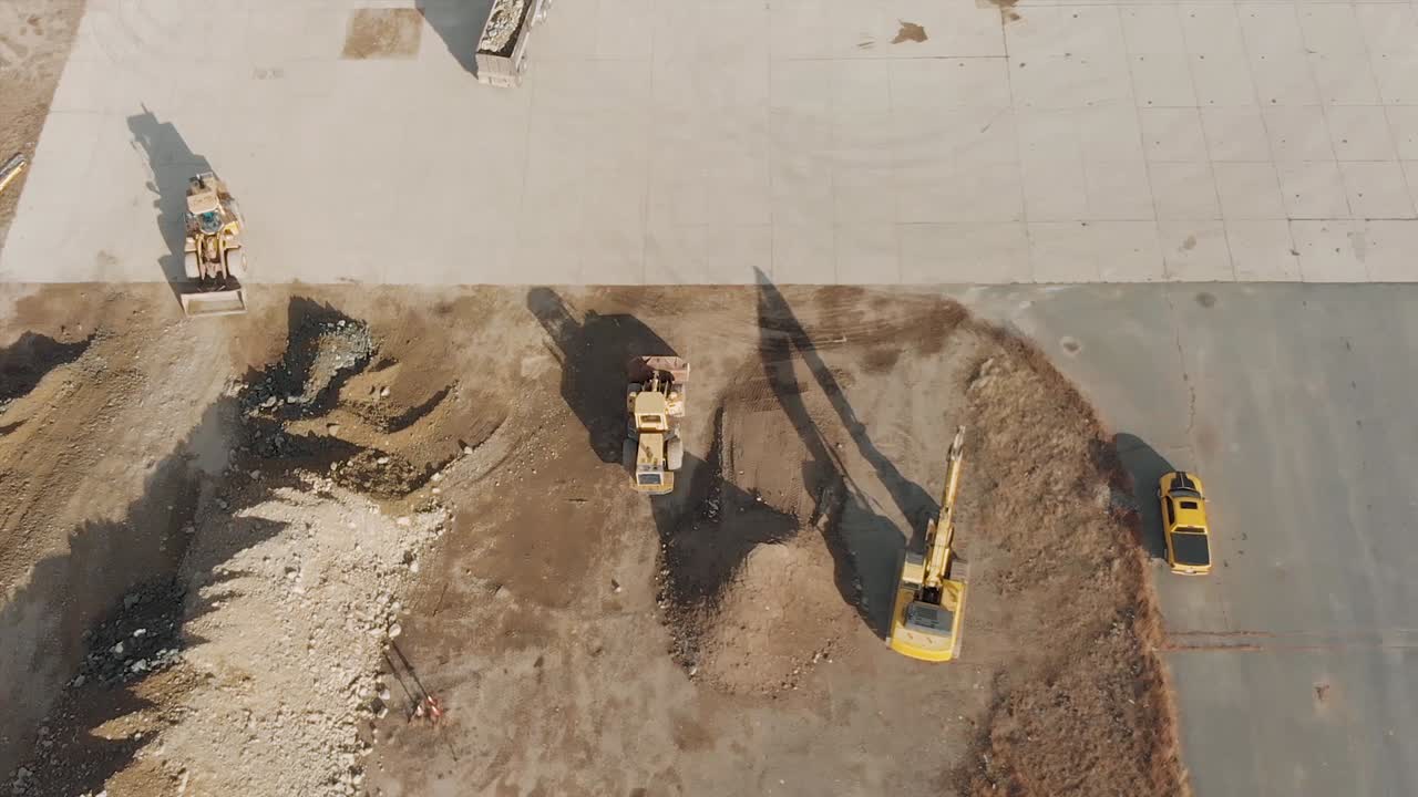 vista de drones a vista de pájaro de vehículos de construcción que mueven tierra alrededor de una plataforma de concreto en un sitio de construcción ocupado durante un día nublado de invierno