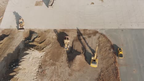 birds-eye drone view of construction vehicles moving dirt around a concrete pad at a busy construction site during a cloudy winter day