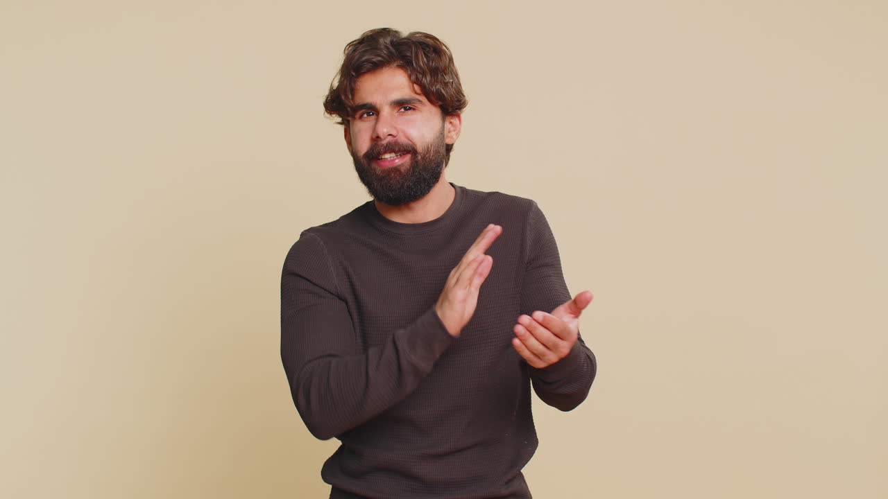 joven libanés mostrando los pulgares hacia arriba y asintiendo con la cabeza en aprobación aplaude las manos contra un fondo beige