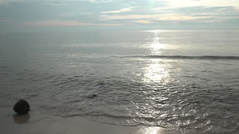 close up shot of a dramatic morning sunrise, the golden rays reflecting of the ocean water as the shallow waves wash up on the sandy beach of cha am, phetchaburi, thailand