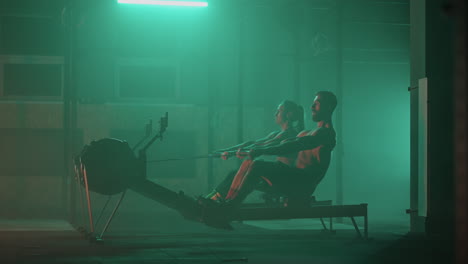 a man and a woman perform strong athletes perform exercises in the gym on a rowing machine in slow motion