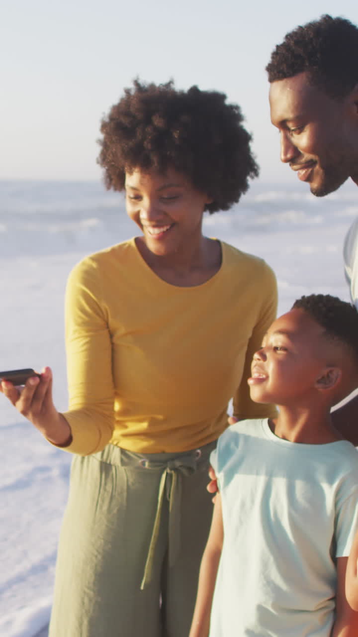 Famiglia afroamericana sorridente che scatta un selfie e si abbraccia su una spiaggia assolata.