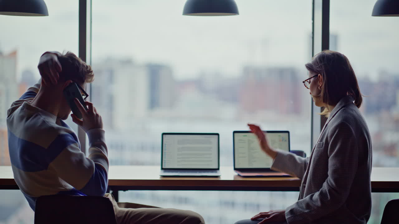 Tensed colleagues calling cellphone at big windows company workplace closeup