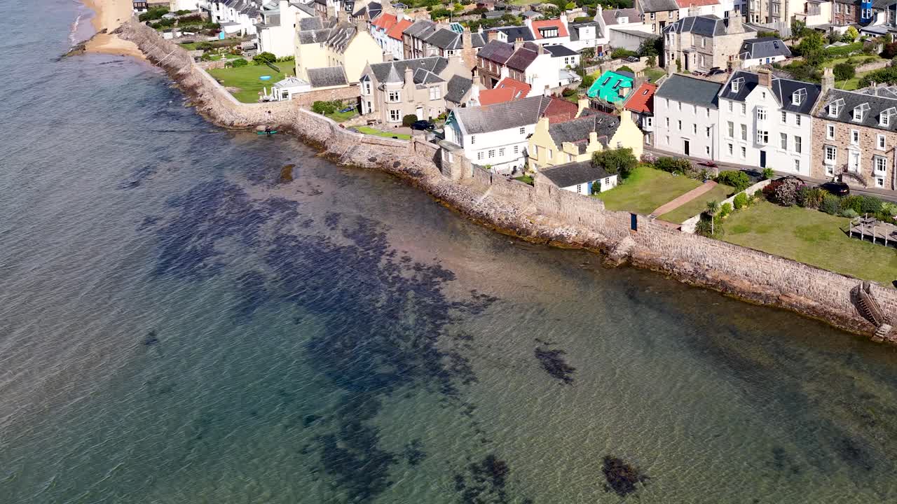 Drone glides above seaside homes, clear shoreline, and waterfront architecture in bright daylight