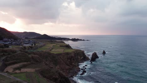 Drone-Kyotango-Serenidad-Puesta-De-Sol-Aérea-Paisaje-Sobre-La-Belleza-Costera-Japonesa-Puesta-De-Sol-Rosa-Puesta-De-Sol-Dorada,-Olas-Azules-Aplastan-El-Acantilado-Peninsular