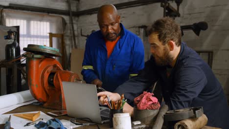 Two-metalsmiths-discussing-over-laptop-on-desk-4k