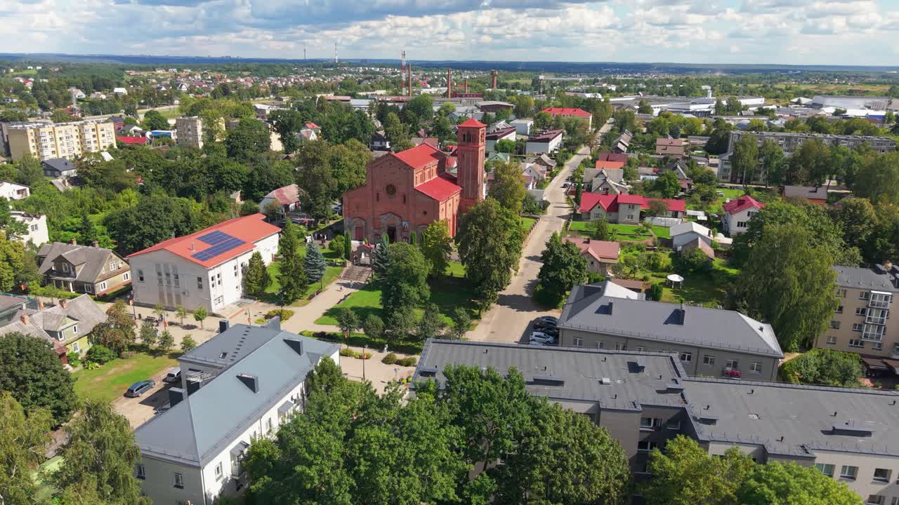 Aerial view of Lentvaris town in Lithuania, featuring the iconic red brick church surrounded by residential buildings and greenery on a bright summer day