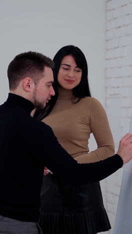 young partners making new business plan. handsome businessman is writing on a white board. beautiful woman talking to a man in the office. vertical video