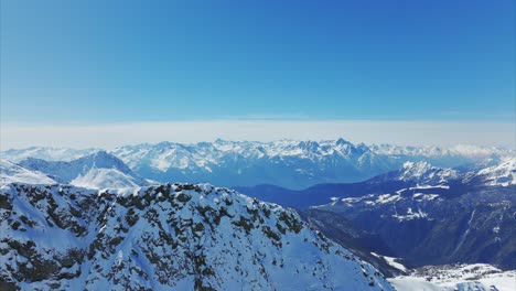 panoramic aerial drone view of snow-covered mountain peaks under clear blue sky in italian alps, vast, majestic winter landscape, italy. copy space