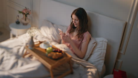 serene woman texting mobile phone in morning. relaxed girl enjoying breakfast