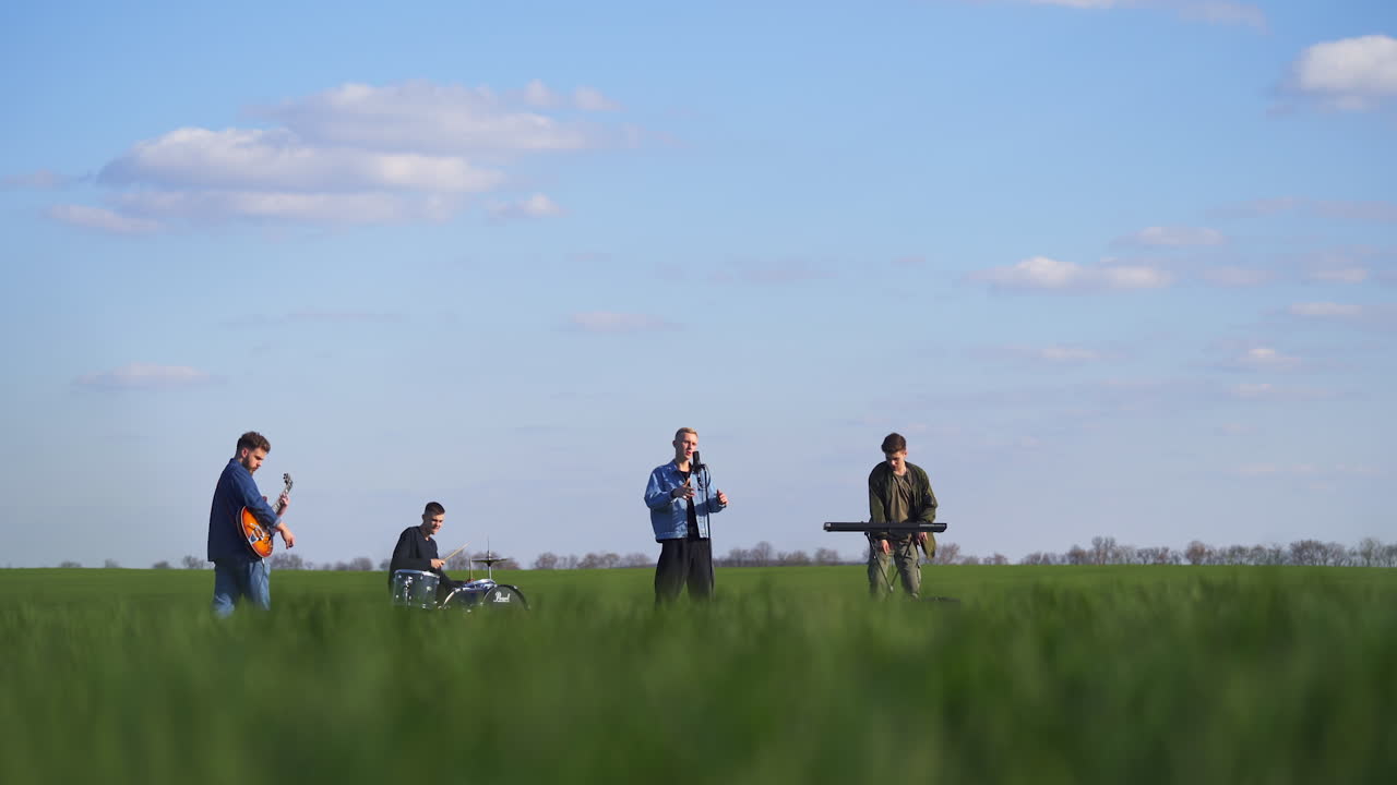 Emotional and active performance of a boys band in the green fields. Music band playing music and sing while drone flying around them.