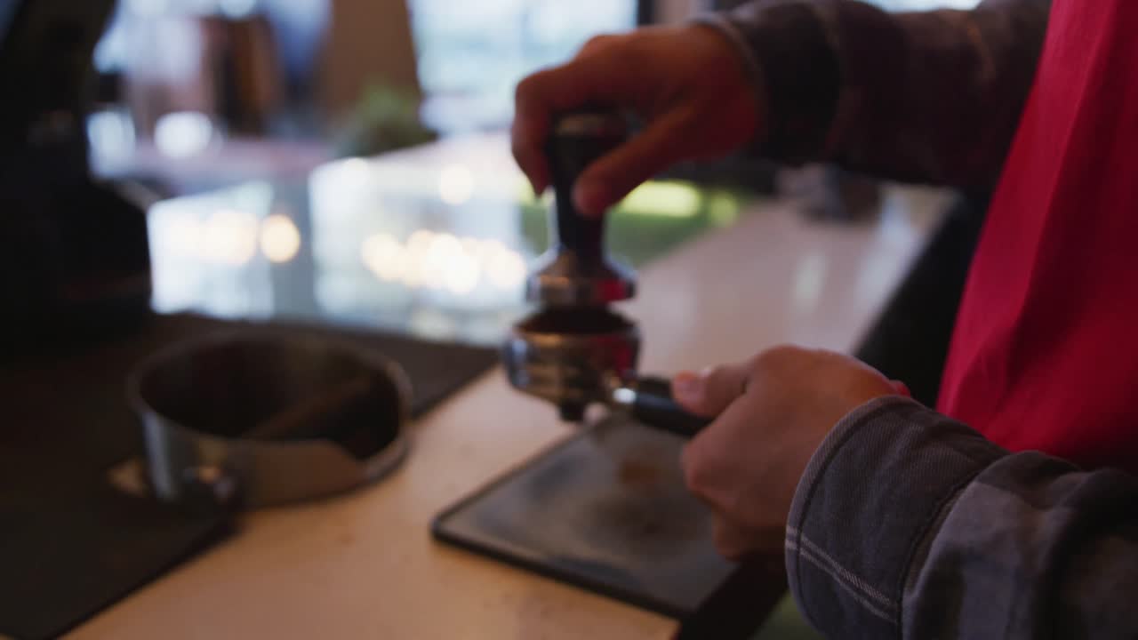 Mani di un barista uomo di etnia mista che indossa un grembiule e prepara caffè da asporto.