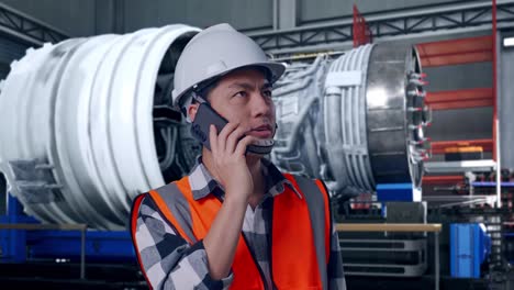 close up of asian male engineer with safety helmet talking on smartphone while standing with airplane engine maintenance conducted, analytics checking the turbine
