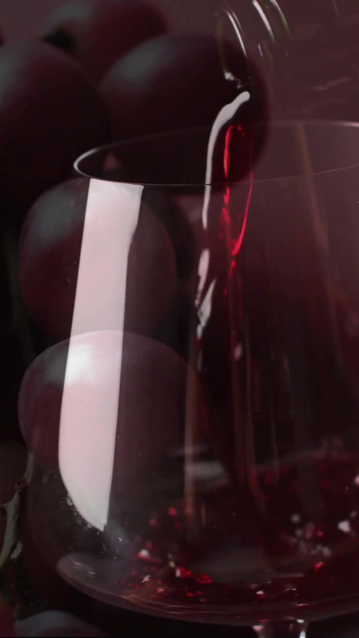 Composizione di vino rosso versato in un bicchiere sopra l'uva su sfondo rosso.
