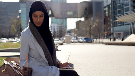 Vista-Lateral-De-Una-Joven-Asiática-Con-Hijab-Usando-Un-Teléfono-Móvil-En-La-Ciudad-4k