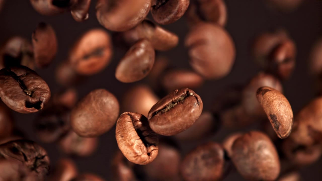 Ristede kaffebønner falder i slowmotion med mørk baggrund