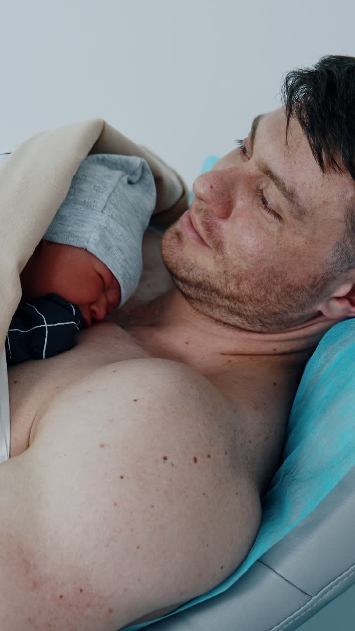 Father is happy to hold and caressing his newborn baby. The child is laid on the dad's chest right after birth. Vertical video