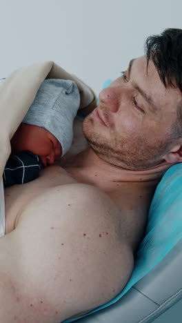 father is happy to hold and caressing his newborn baby. the child is laid on the dad's chest right after birth. vertical video