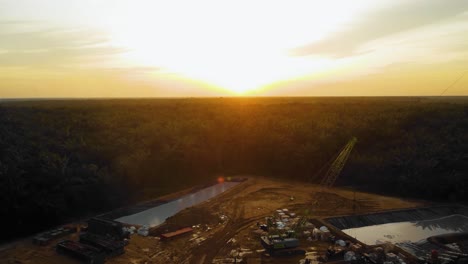 Cinematic-4K-Drone-Footage-of-Onshore-Drilling-Rig-equipment-structure-for-oil-exploration-and-exploitation-in-the-middle-of-jungle-surrounded-by-palm-oil-trees-during-sunset-and-high-oil-price