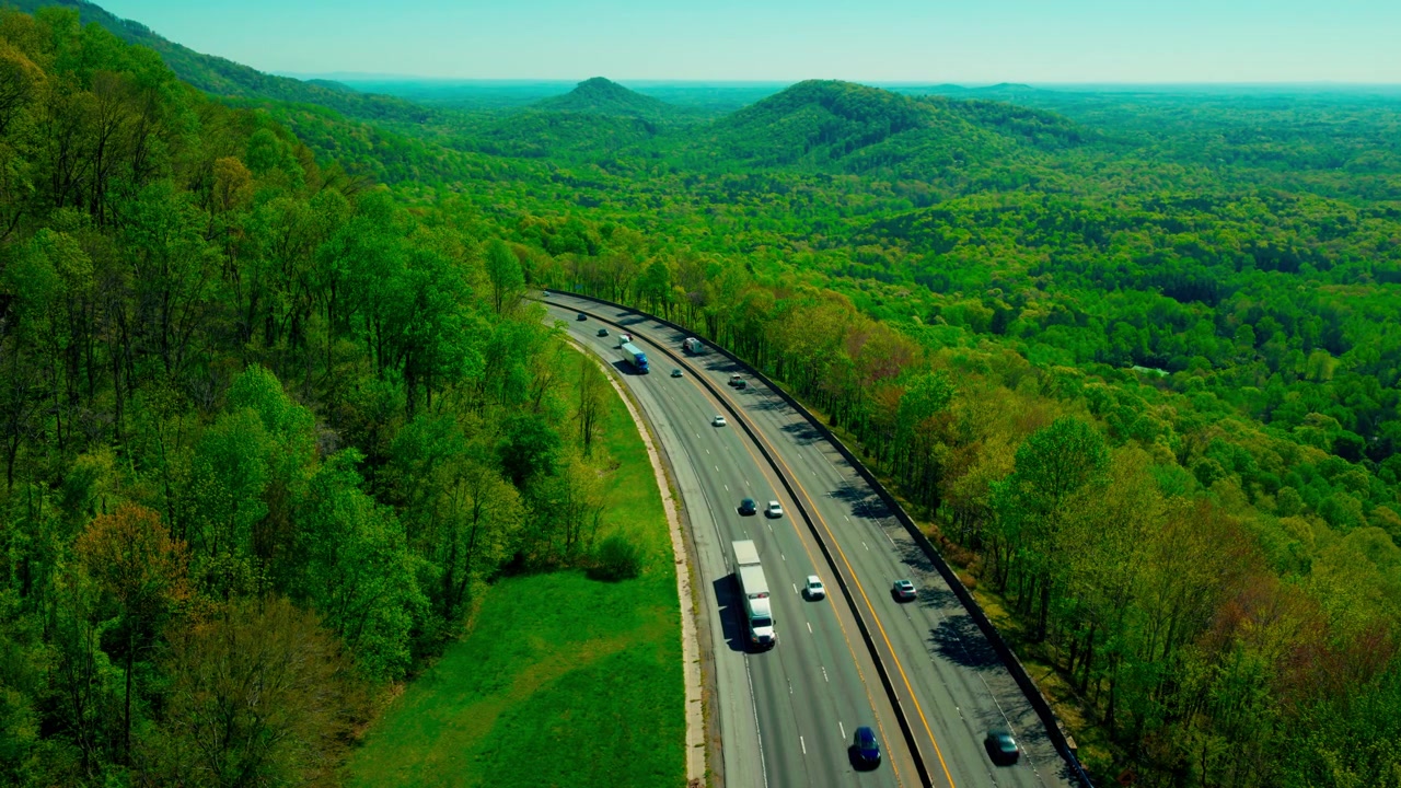 High-angle view of commercial semi-trucks navigating the winding Andrew Jackson Highway near Troy, North Carolina. The backbone of the Southeast shipping corridor.