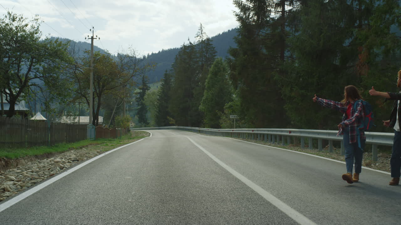 Turisti felici fanno l'autostop in autostrada. Amici sorridenti salutano nella natura.