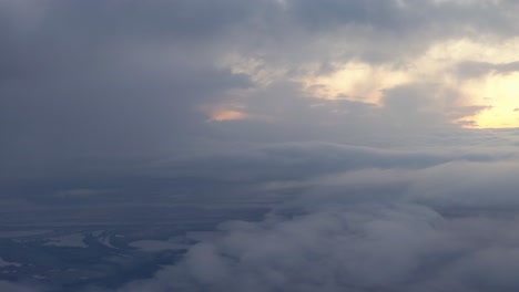 Looking-out-an-airplane-window-at-golden-sunrise-while-descending-through-dense-clouds