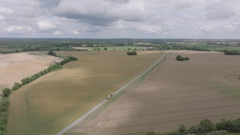 Vista-Of-Country-Road-In-Farmlands-With-Wind-Turbines-In-The-Background