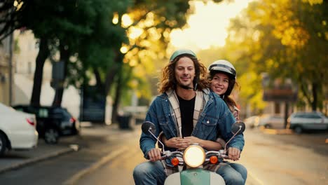 A-happy-guy-in-a-green-moped-helmet-with-long-curly-hair-and-a-blue-denim-jacket-arrived-and-stopped-with-his-happy-girlfriend-in-a-White-helmet-on-a-green-moped-in-a-city-street-on-the-road-in-the-morning-in-the-summer