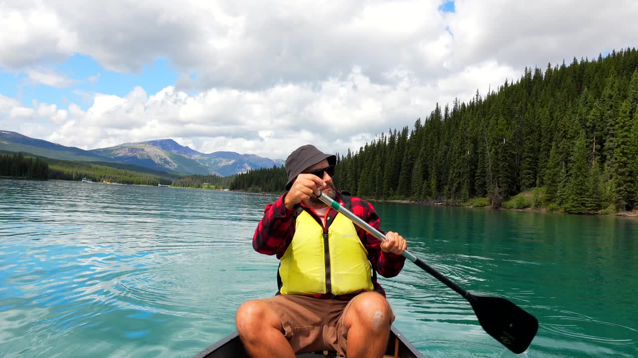 Uomo in canoa su un lago circondato da foreste e montagne