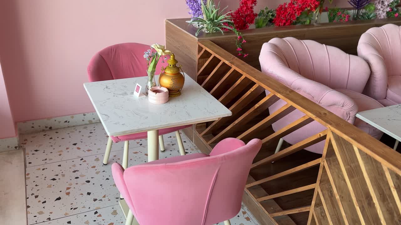 Intérieur de café rose élégant avec des chaises rembourrées, une table à plateau en marbre, des fleurs décoratives et une cloison en bois, capturé sous un éclairage intérieur doux avec une ambiance moderne et chaleureuse.