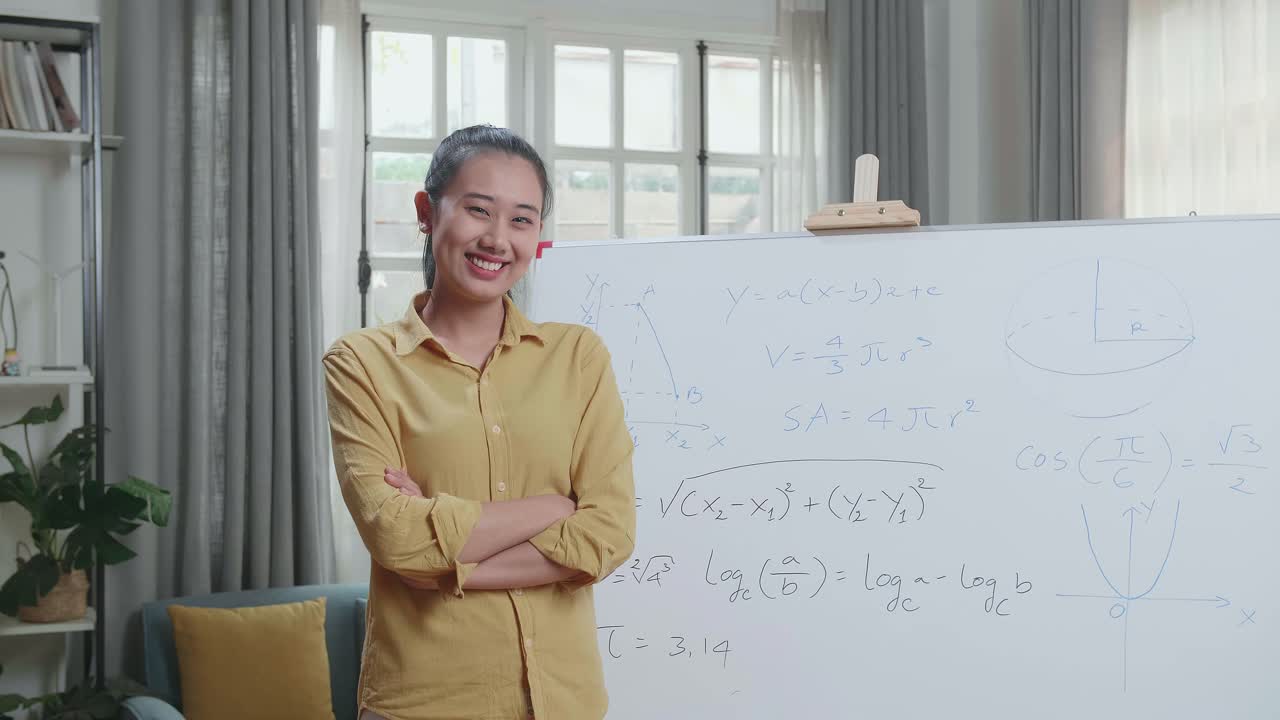 自宅で数学を教えながら、腕を組みカメラに微笑みかけるアジア人女性教師