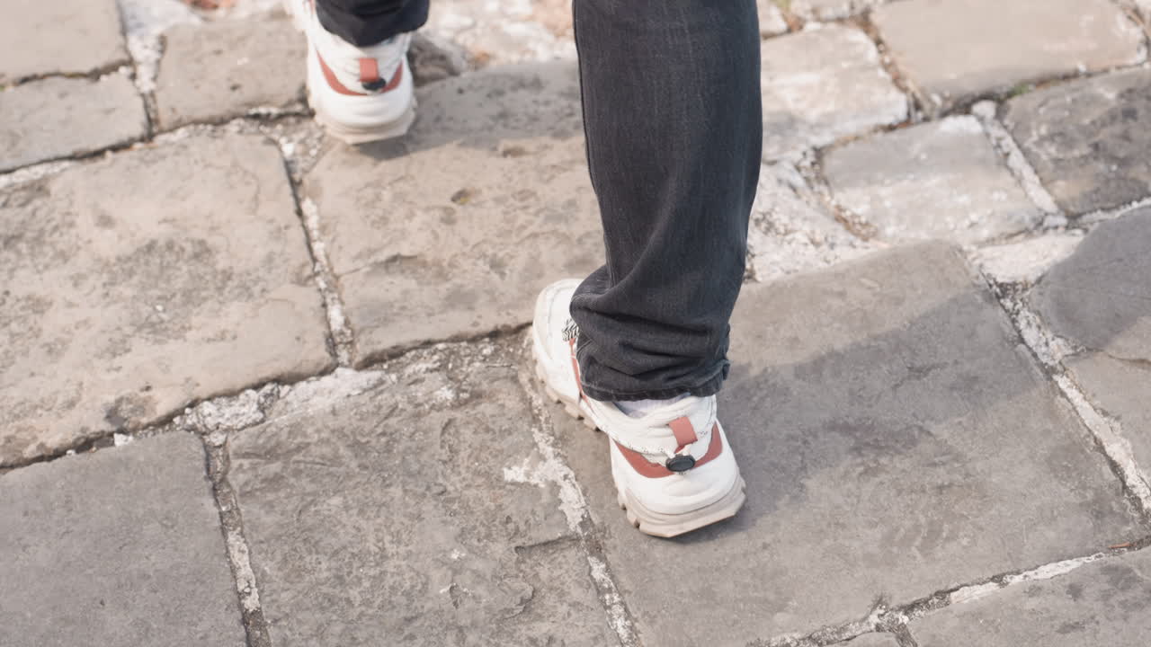 Closeup of sneakers walking on stone pavement, white patterned shoes stepping over weathered cobblestones with crevices and moss, rhythmic stride and balanced motion, texture details and ground