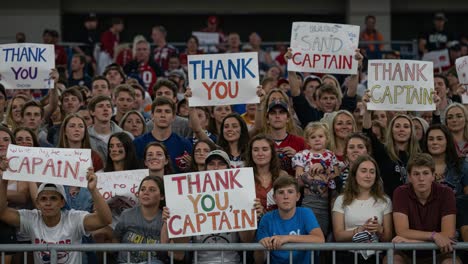 cheering crowd displays gratitude with colorful signs reading 'thank you captain' amidst excitement and team spirit in an energetic atmosphere
