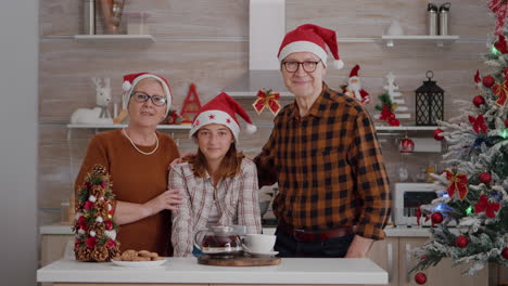 portrait of happy family wearing santa hat looking into camera standing at table in xmas decorated kitchen