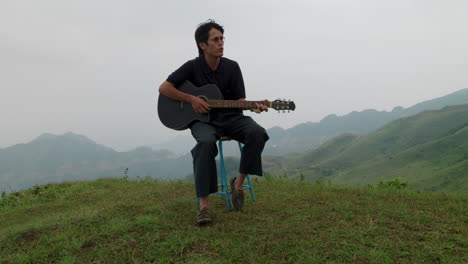 front view of young adult playing black guitar in middle of exotic green hilltop