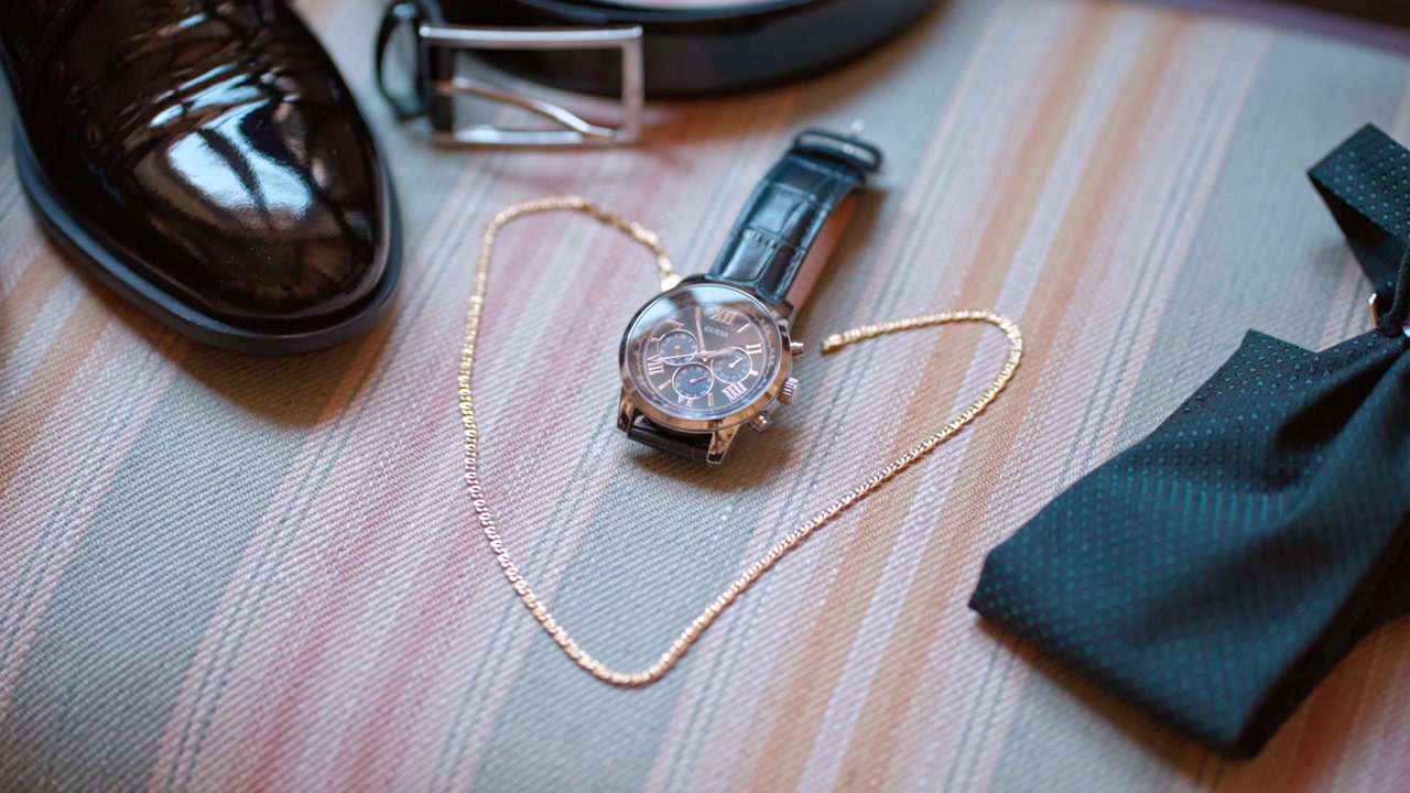 Elegant watch, shoes, tie for a formal event setup on a striped surface